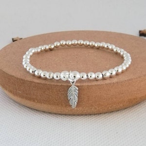 May include: A silver beaded bracelet with a small silver feather charm.
