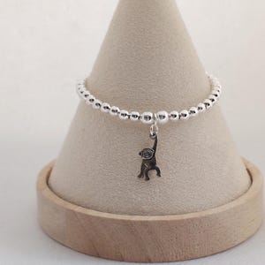 May include: A silver-toned beaded bracelet featuring a small, dangling monkey charm. The bracelet is composed of numerous polished, spherical beads strung together, with a single monkey-shaped pendant hanging from the centre of the chain.