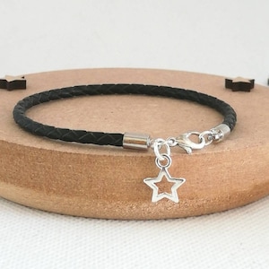 May include: A black leather bracelet with a silver star charm. The bracelet is braided and has a silver clasp.