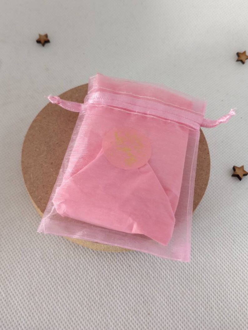 May include: A pink organza gift bag with a gold sticker that says "Little Things" on it. The bag is tied with a pink ribbon.