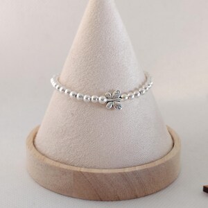 May include: A silver beaded bracelet with a butterfly charm. The bracelet is displayed on a light beige cone-shaped stand with a wooden base. The butterfly charm is centered on the bracelet.