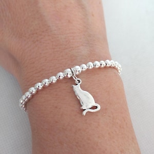 May include: A silver beaded bracelet with a silver charm of a cat sitting down.