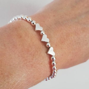 May include: A silver bracelet with small round beads and heart-shaped charms.