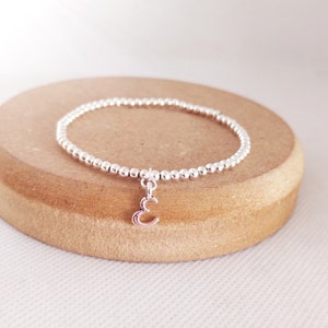 May include: A silver beaded bracelet with a silver charm in the shape of the letter 'E'.