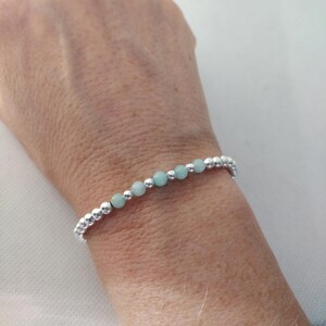 May include: A delicate bracelet with alternating silver and light blue beads. The bracelet is on a person's wrist.