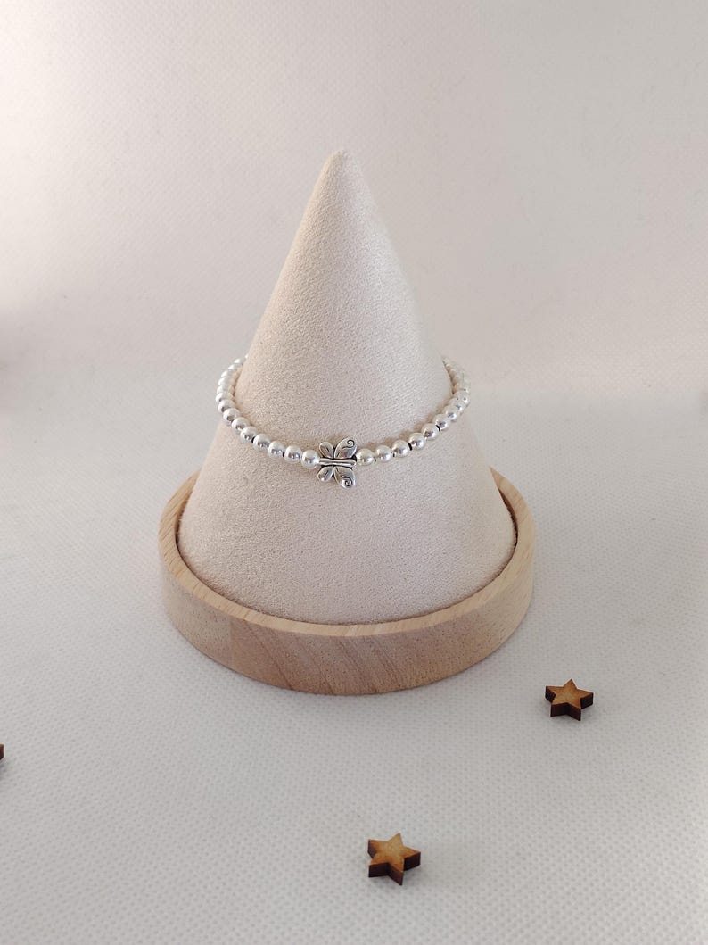 May include: A silver beaded ring with a four-leaf clover charm is displayed on a beige cone-shaped stand. The ring is made of small, round silver beads. The stand sits on a wooden base, with small wooden star decorations scattered around.