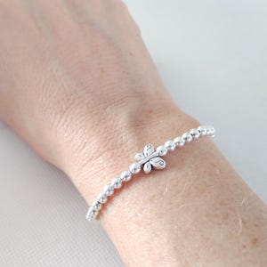 May include: A silver beaded bracelet with a butterfly charm. The bracelet features small, round beads strung together with an elastic band. The butterfly charm is centered on the bracelet and has a detailed design.
