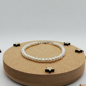 May include: A white pearl bracelet with a silver clasp. The bracelet is on a brown wooden surface.