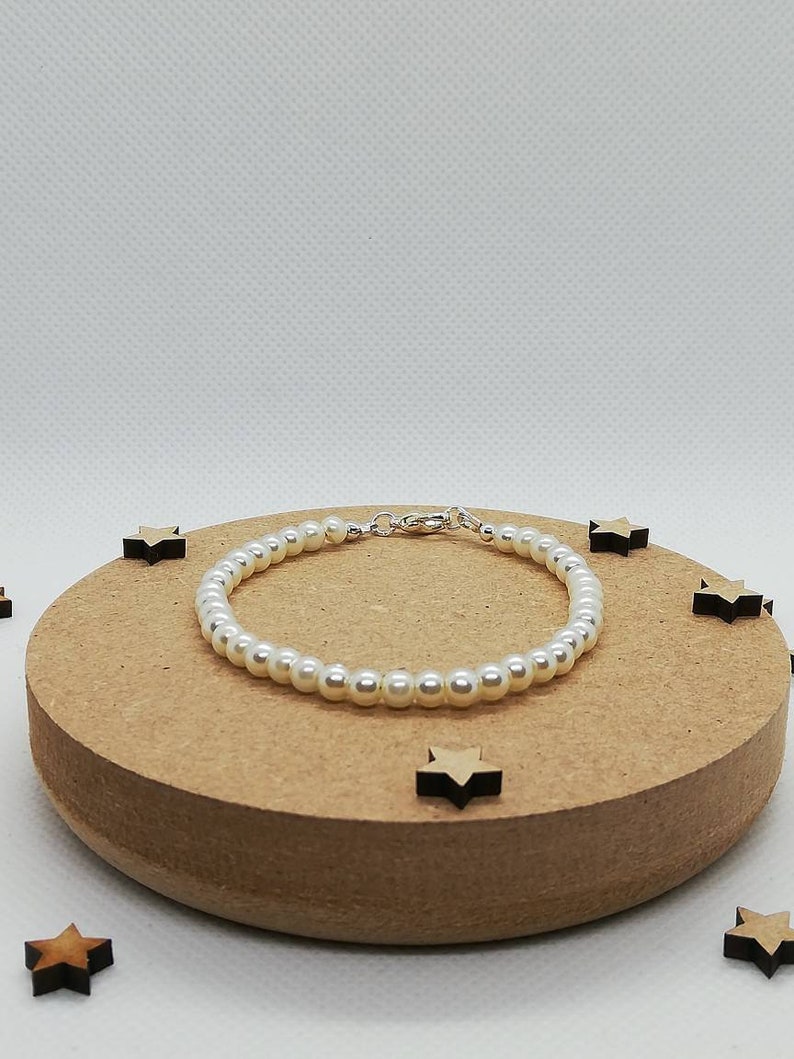 May include: A white pearl bracelet with a silver clasp. The bracelet is on a brown wooden surface.
