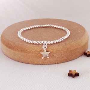 May include: A silver beaded bracelet with a star charm. The bracelet is on a wooden surface.