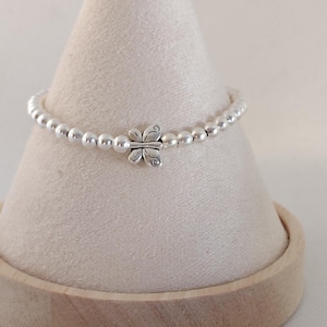 May include: A silver beaded bracelet with a butterfly charm. The bracelet features small, round silver beads and a detailed butterfly pendant at the center. The bracelet is displayed on a light-colored, cone-shaped stand.