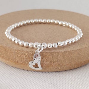 May include: A silver bracelet with a small, hammered heart charm. The bracelet is made of tiny silver beads.