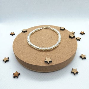 May include: A white pearl bracelet with a silver clasp. The bracelet is on a wooden surface with small wooden stars scattered around it.