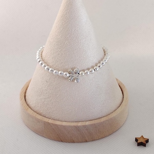 May include: A silver beaded bracelet with a butterfly charm. The bracelet is displayed on a white cone-shaped stand with a wooden base. Two small wooden star-shaped decorations are placed near the base.