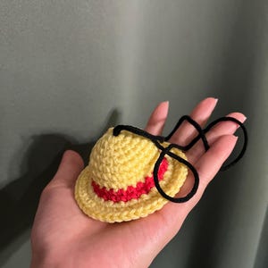 May include: A small yellow crocheted hat with a red band and a black string.