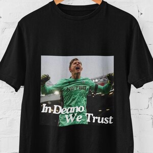 May include: Black t-shirt with a photo of a soccer player in a green and black uniform with the text "In Deano We Trust" printed on the front.