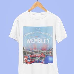 May include: White t-shirt with a graphic print of Wembley Stadium. The graphic features the stadium's arch, the words "Wembley" and "South London & Proud", and red and blue balloons. The shirt has a crew neck and short sleeves.