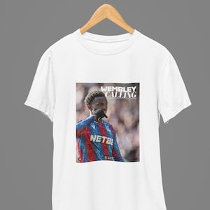 May include: White t-shirt with a graphic print of a soccer player wearing a blue and red jersey with the text "Wembley Calling" and "NETBET" on it.