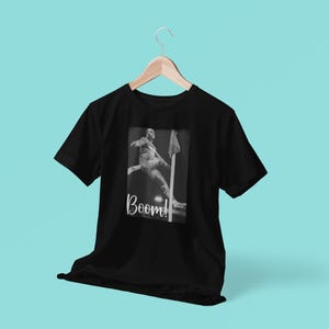 May include: Black t-shirt with a graphic of a person jumping over a hurdle. The graphic is in black and white and the text "Boom!" is printed below the graphic.