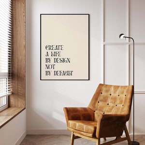 May include: A black framed poster with the text "CREATE A LIFE BY DESIGN NOT BY DEFAULT" hanging on a white wall in a room with a brown leather armchair and a floor lamp.