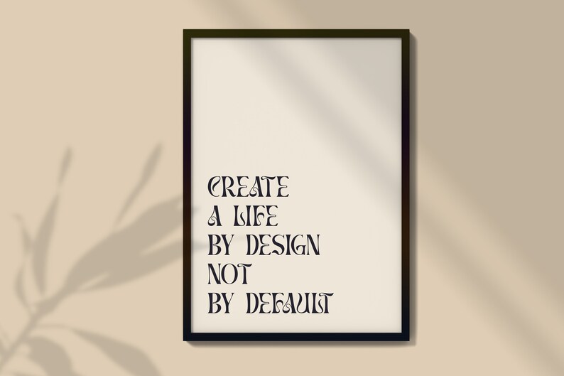 May include: A black framed print with the text "CREATE A LIFE BY DESIGN NOT BY DEFAULT" on a beige background.
