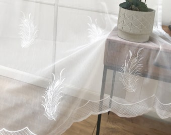 Könnte beinhalten: Transparenter weißer Vorhang mit gesticktem Federdesign. Der Vorhang hat einen gewellten unteren Rand. Eine Topfpflanze mit grünen Blättern steht auf einem kleinen Tisch.