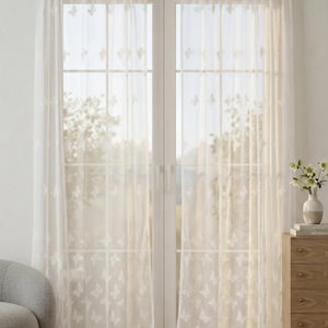 Puede incluir: Un par de cortinas blancas transparentes con un patrón de mariposas bordadas por toda la superficie. La tela ligera cuelga de una barra y cubre un juego de puertas dobles de cristal. Las cortinas tienen una textura delicada y bordes festoneados.