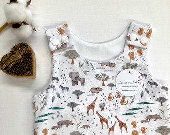 May include: White baby onesie with a jungle animal print. The onesie has a white background with brown, orange, and green animals, including giraffes, elephants, zebras, lions, and hippos. The onesie has a white tag with the text "Diane's wee darlings Handmade in Scotland www.dianesweedarlings.com".