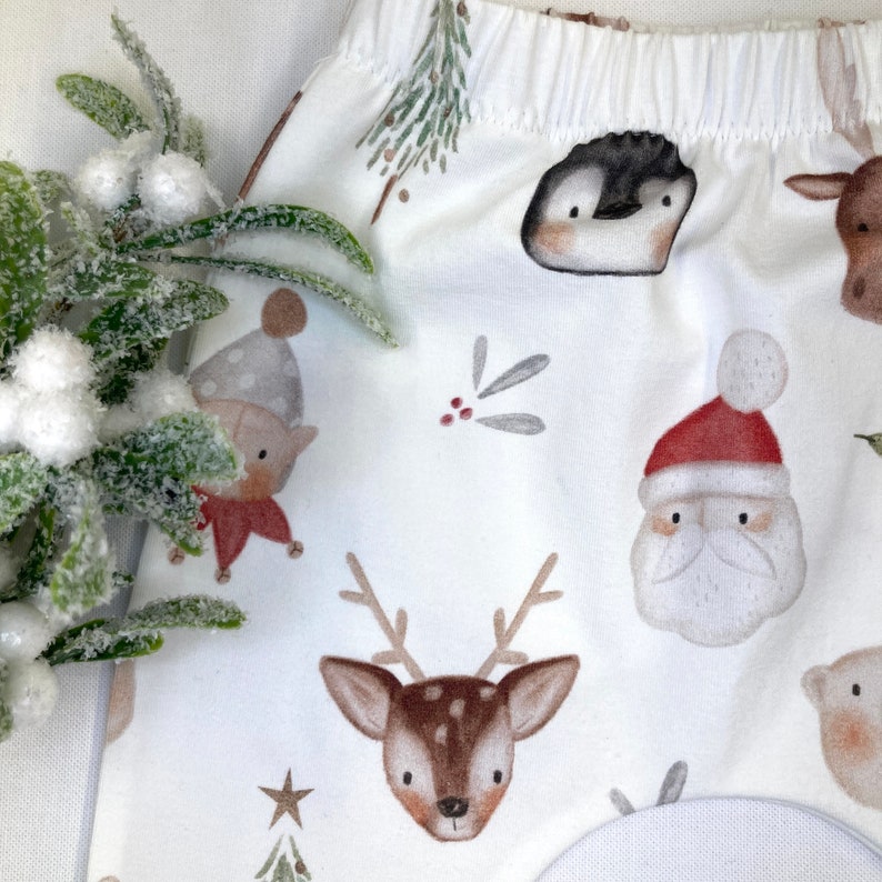 Puede incluir: Tela blanca con un estampado repetido de tem&aacute;tica navide&ntilde;a. El dise&ntilde;o incluye ilustraciones de Pap&aacute; Noel, renos, ping&uuml;inos y elfos. La tela tambi&eacute;n presenta peque&ntilde;os &aacute;rboles de Navidad y estrellas.