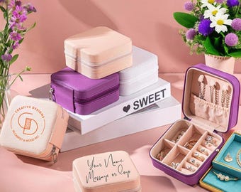 May include: A collection of jewelry boxes in various colors, including pink, purple, and white. Some boxes are closed, while others are open, revealing rings and necklaces. The boxes are arranged on a white platform with the word "SWEET" on it.
