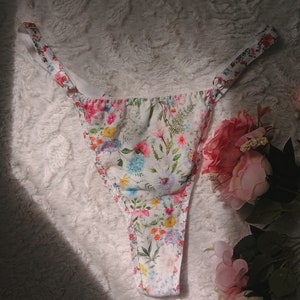 Può includere: Intimo in pizzo floreale bianco con spalline regolabili. L'intimo presenta un delicato motivo floreale con fiori rosa, gialli e blu.