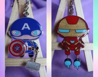 May include: Two keychains featuring cartoon characters from the Marvel Cinematic Universe. The first keychain features Captain America with a red, white, and blue color scheme and a shield. The second keychain features Iron Man with a red, gold, and silver color scheme and a repulsor beam.