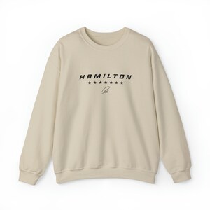 Peut inclure: Un sweat-shirt beige avec un imprimé graphique noir qui dit "HAMILTON" avec sept étoiles et une signature.