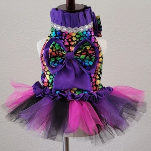 May include: A purple and black tutu with a rainbow print and a large purple bow. The tutu has a black and pink tulle skirt.