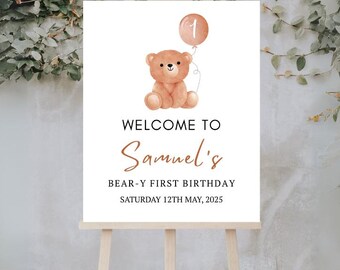 May include: A welcome sign on a wooden easel features a teddy bear holding a balloon. The sign reads "Welcome to Samuel's Bear-y First Birthday Saturday 12th May, 2025". The sign is white with brown text and a watercolor illustration.