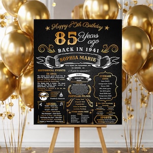 Puede incluir: Un letrero de cumpleaños negro y dorado sobre un caballete, rodeado de globos dorados. El letrero dice "Feliz 85 cumpleaños" e incluye detalles sobre el año 1941, como eventos históricos, películas populares y costos promedio. El letrero es para Sophia Marie.
