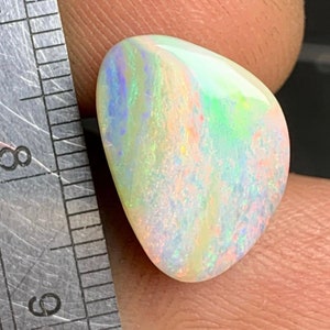 May include: A white opal gemstone with a teardrop shape and iridescent rainbow colors. The opal is approximately 1 inch in length.