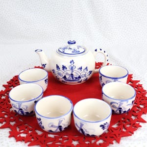 Könnte beinhalten: Ein blaues und weißes holländisches Teeset mit einer Teekanne und sechs Tassen. Die Teekanne und die Tassen sind mit einer Windmühle und Blumenmustern verziert.