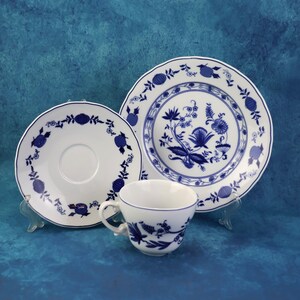 May include: A white porcelain teacup, saucer, and two plates with a blue floral design. The teacup has a curved handle. The plates and saucer have a scalloped edge. The background is a solid blue.