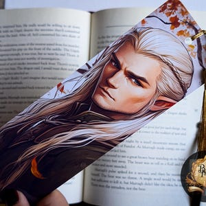May include: A bookmark featuring a detailed illustration of a man with long white hair and blue eyes. He is wearing a dark jacket and has a serious expression. The background is a blurred image of autumn leaves.