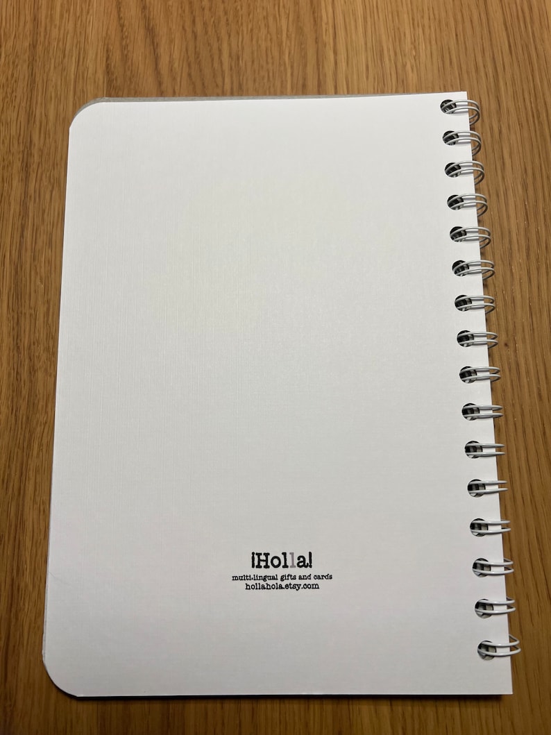 Pu&ograve; includere: Un quaderno bianco a spirale con il testo "&iexcl;Holla!" e "multi-lingual gifts and cards hollahola.etsy.com" stampato sulla copertina posteriore.