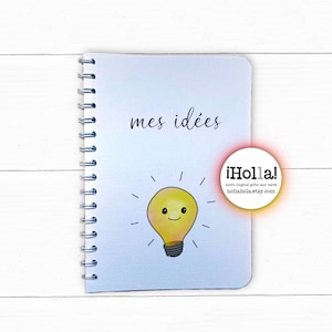 An A5 wire bound white notebook with Mes idées in a lowercase moden swirly handwritten font above a smiling illuminated lightbulb looking rather pleased with itself. Hollahola.etsy.com logo is in a circle on the right hand side.