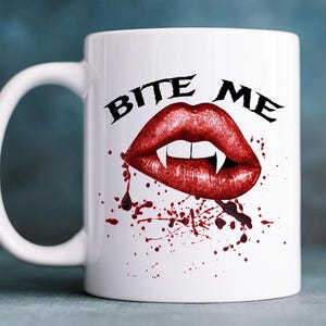 Peut inclure: Mug en céramique blanche avec le texte noir "BITE ME" et un dessin de lèvres rouges avec des crocs. Le design comprend des éclaboussures de sang rouge, créant une esthétique effrayante et gothique.