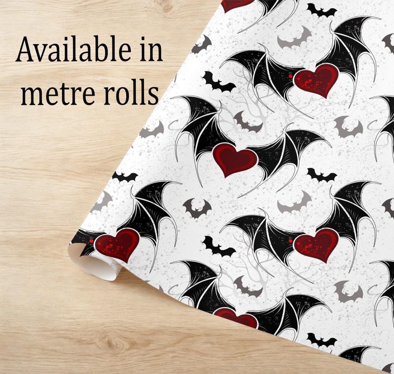 May include: A roll of white wrapping paper featuring a repeating pattern of red hearts with black bat wings, small black bats, and grey silhouettes. The text "Available in metre rolls" is printed in black on the upper left side of the paper.