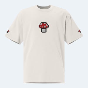 May include: White t-shirt with a red and white pixelated mushroom graphic on the front.