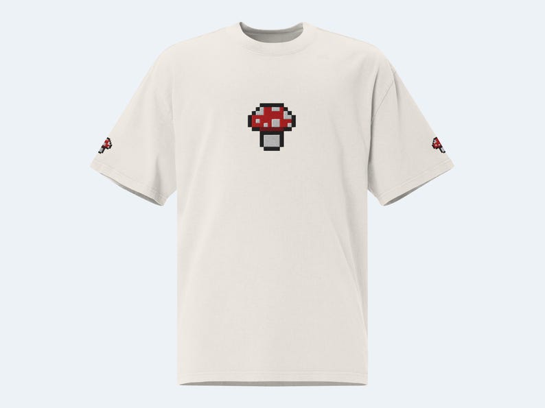 May include: White t-shirt with a red and white pixelated mushroom graphic on the front.