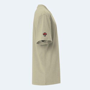 May include: A beige short-sleeved t-shirt with a red and white mushroom graphic on the sleeve.