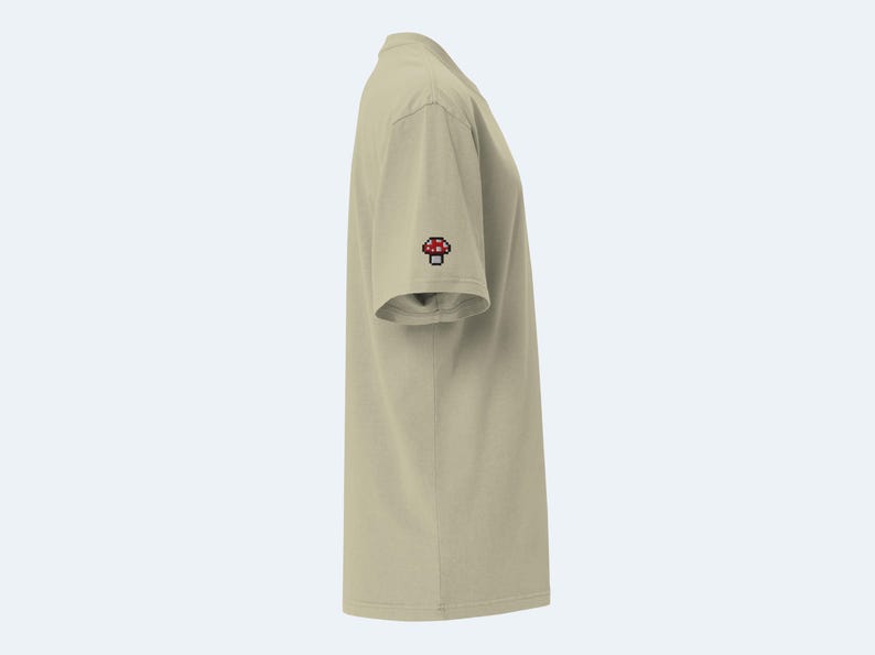 May include: A beige short-sleeved t-shirt with a red and white mushroom graphic on the sleeve.
