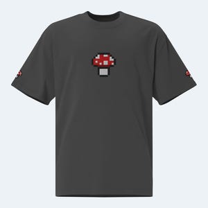 May include: A dark gray t-shirt with a pixelated red and white mushroom graphic on the front.