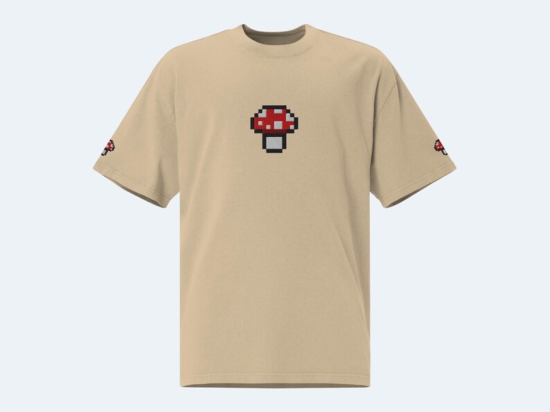 May include: A beige t-shirt with a pixelated red and white mushroom graphic on the front.